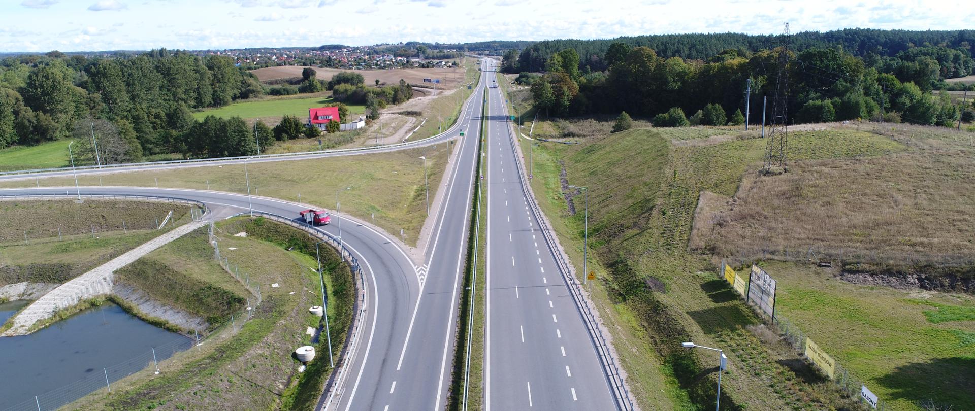 Zdjęcie ilustracyjne obwodnicy. W centrum zdjęcia droga z pojazdami z fragmentem łącznicy węzła po lewej stronie.