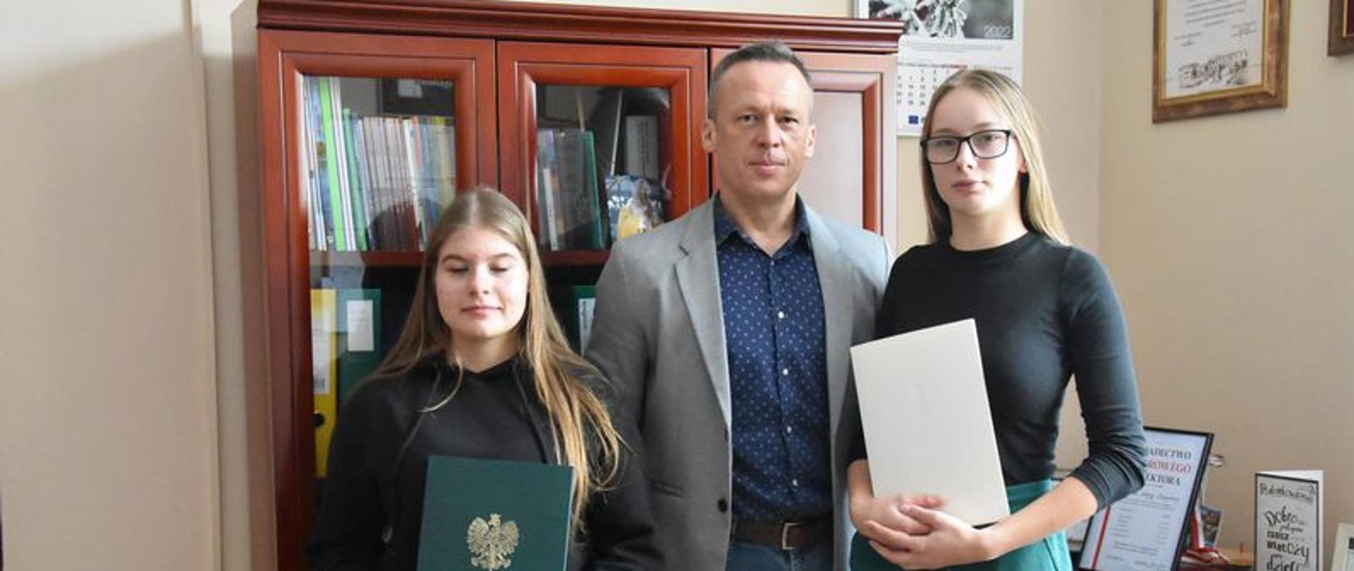 Dyrektor wraz z dwoma uczennicami trzymającymi dyplomy