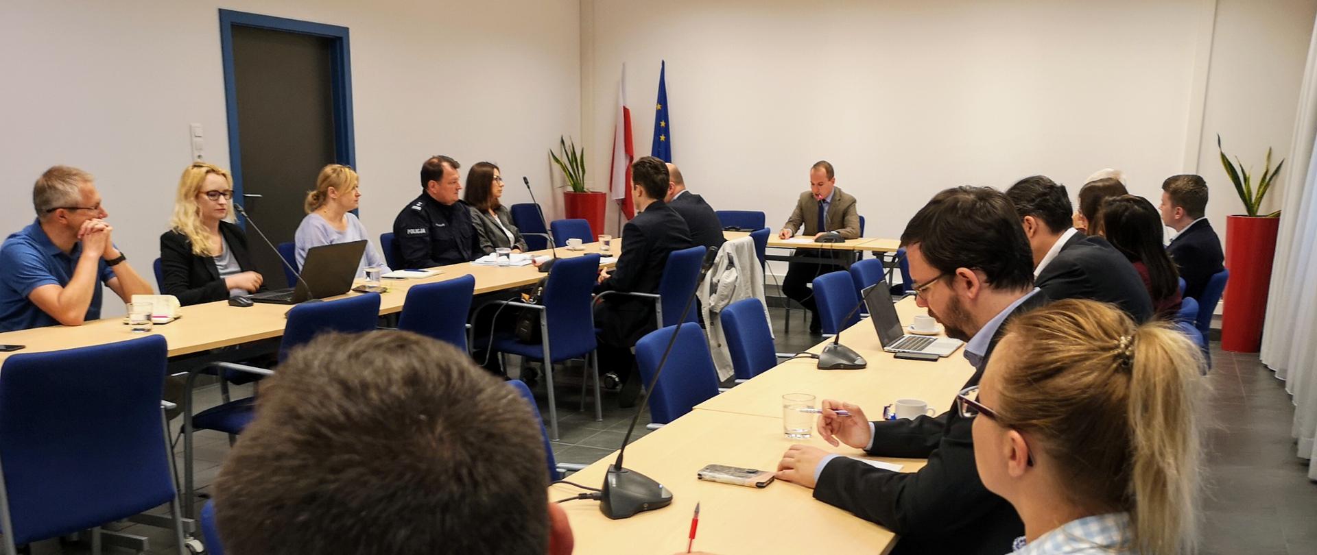 Sala konferencyjna. Przy stolikach siedzi kilkanaście osób.