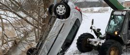 Zielony ładowaczy wyciąga samochód osobowy z rzeki, ziemia pokryta śniegiem.