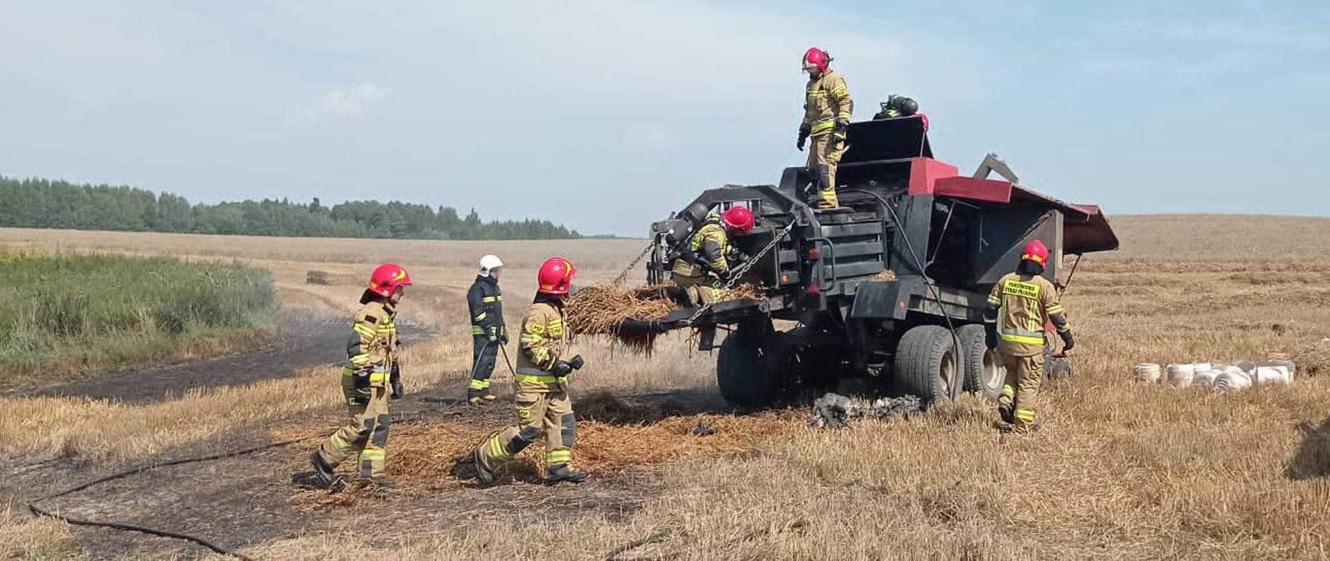 Strażacy na polu gaszą maszynę kostkującą. 