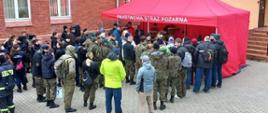 Grupa osób stojąca przed namiotem z napisem Państwowa Straż Pożarna