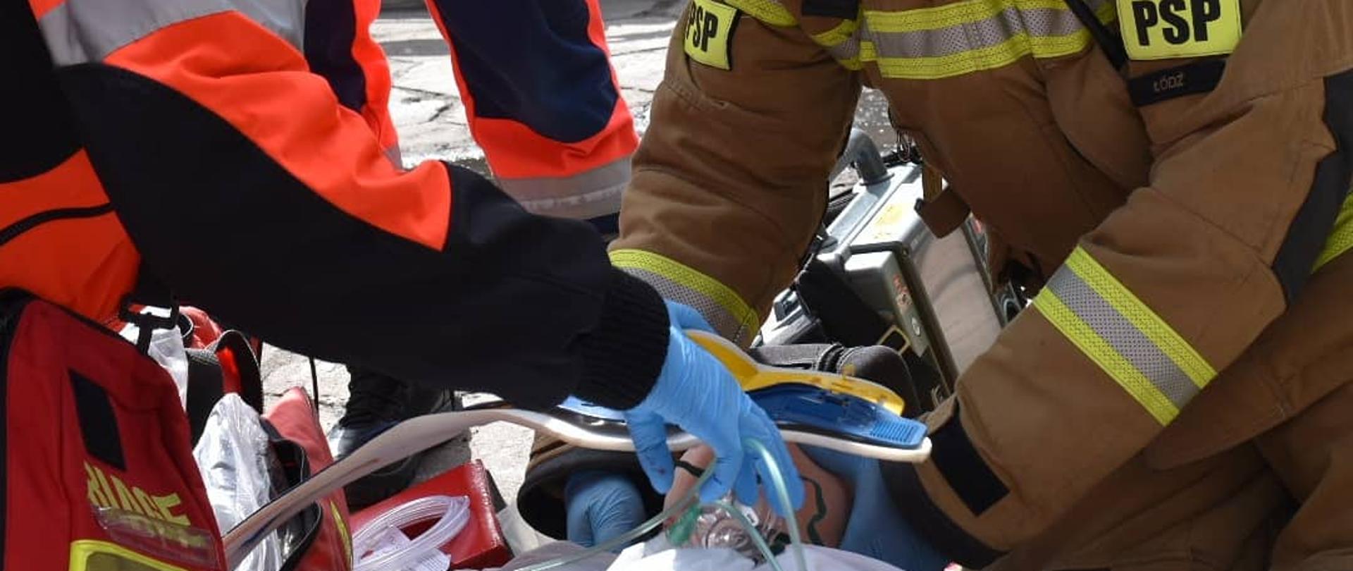 Strażak i ratownik medyczny udzielają pierwszej pomocy poszkodowanej