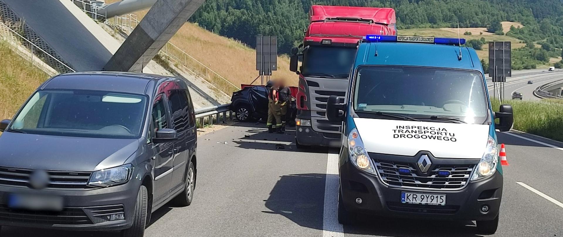 Na pierwszym planie (od lewej) nieoznakowany radiowóz Policji i oznakowany radiowóz małopolskiej ITD typu furgon. W tle ciężarówka i rozbity samochód osobowy.