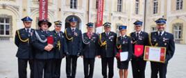 Strażacy stoją po wyróżnieniach na obchodach wojewódzkich dnia strażaka. W tle widać ściany kompleksu pałacowego.