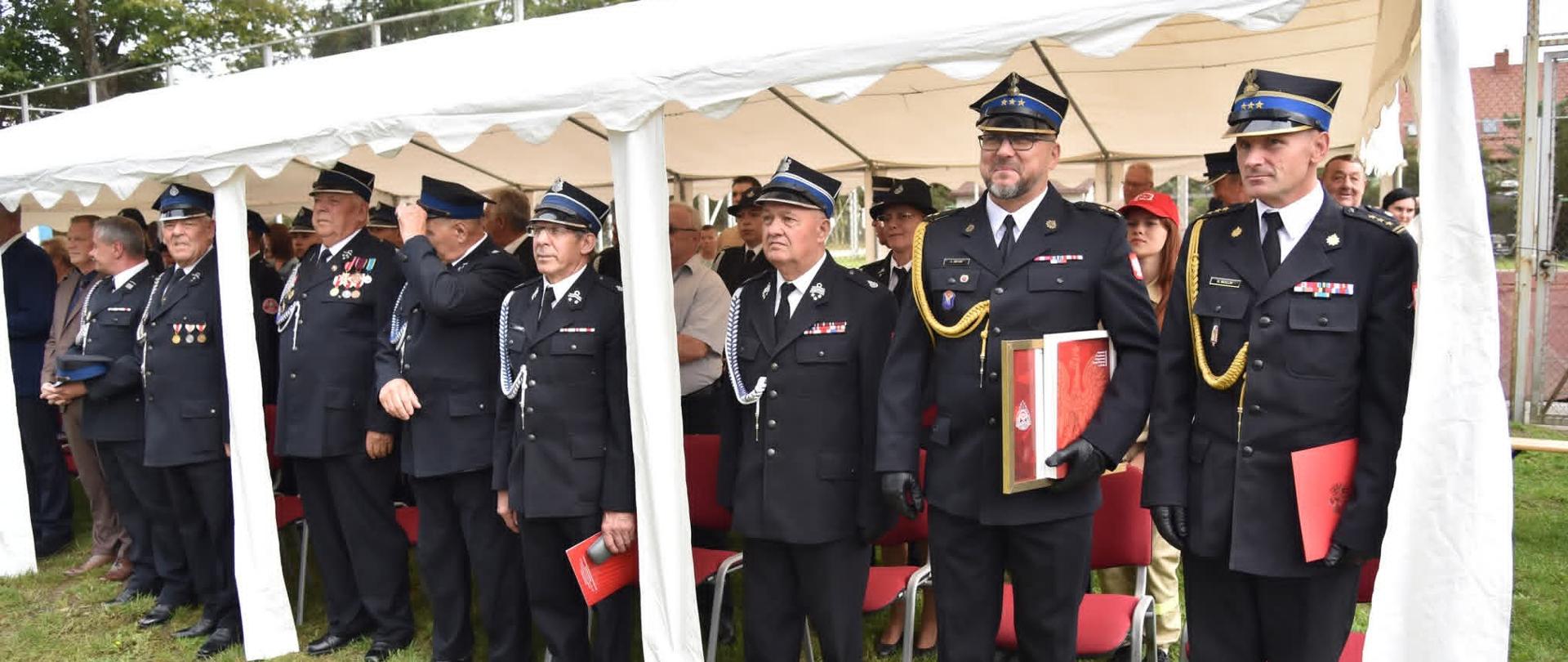 Na zdjęciu Z-ca Pomorskiego Komendanta Wojewódzkiego PSP w Gdańsku st. bryg. Bartłomiej Mollin oraz Z-ca Komendanta Powiatowego PSP w Pucku kpt. Krzysztof Minga. Na zdjęciu również przedstawiciele druhowie OSP. Panowie Komendanci ubrani w mundury galowe PSP. 