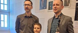 Zdjęcie przedstawia ucznia wraz z wykładowcą oraz nauczycielem prowadzącym zajęcia podczas Międzynarodowej Konferencji Klarnetowej ClariCamp w Poznaniu.