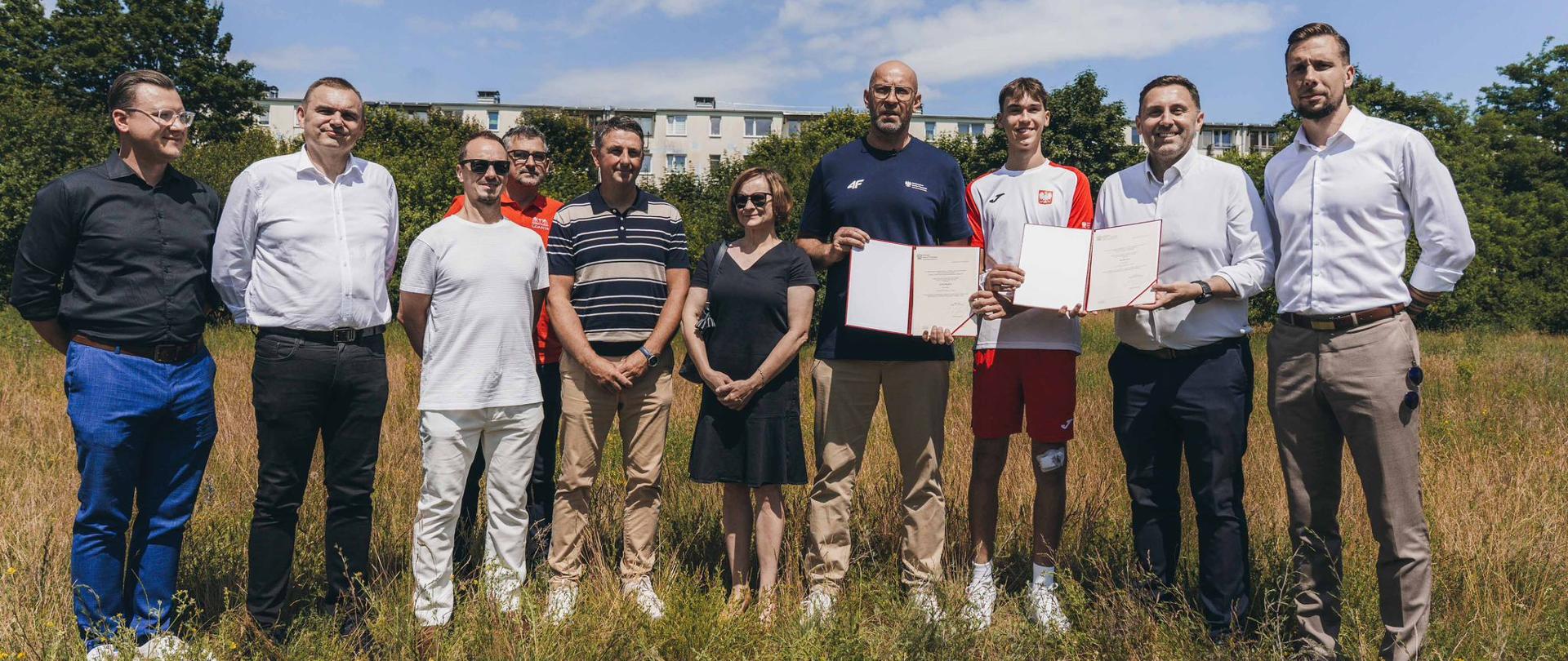 Minister sportu i turystyki Jakub Rutnicki i 9 innych osób stoją na polu prezentując decyzję o dofinansowaniu budowy I etapu Gdańskiego Centrum Tenisa z Programu modernizacji kompleksów tenisowych 