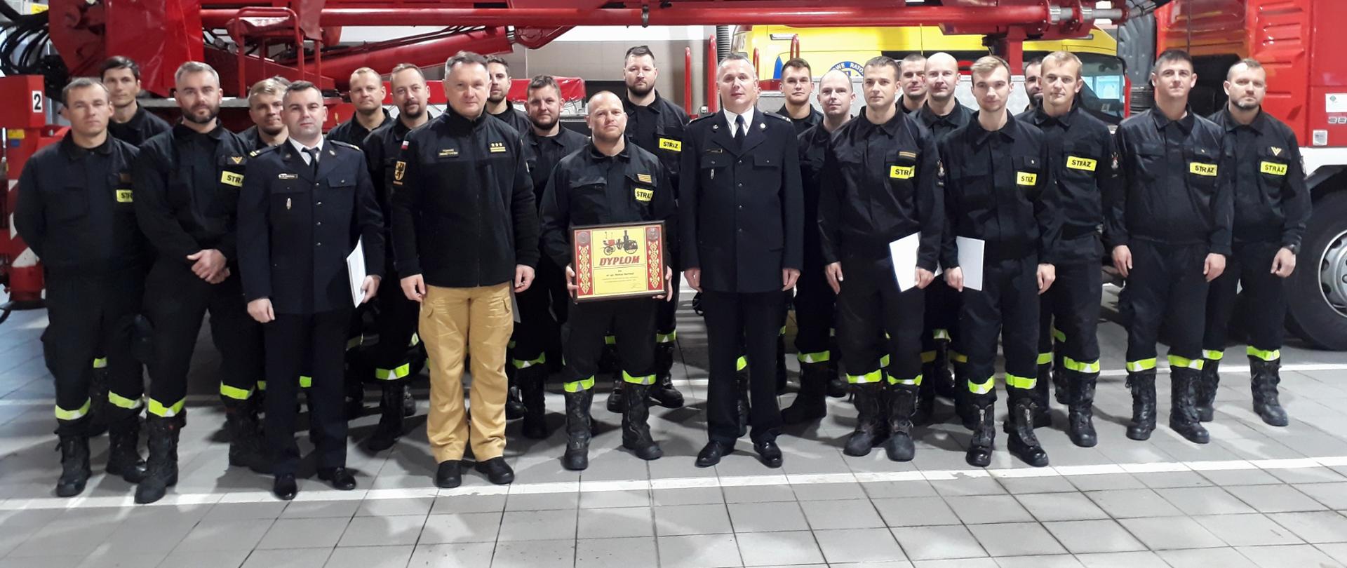 Zastępca pomorskiego komendanta wojewódzkiego Państwowej Straży Pożarnej stoi z funkcjonariuszami Komendy Miejskiej Państwowej Straży Pożarnej w Gdańsku.