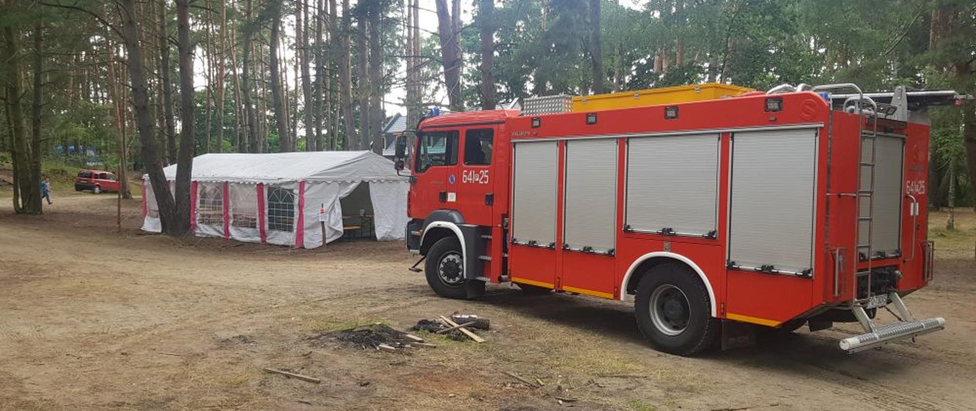 Na pierwszym planie ciężki samochód ratowniczo-gaśniczy wolsztyńskich strażaków, przygotowany do ewentualnego wyjazdu. W tle namioty harcerskie oraz las.