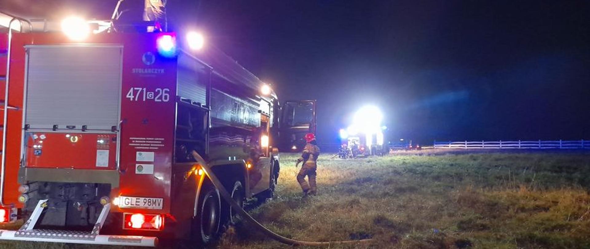 Zdjęcie przedstawia oświetlony przez najaśnice teren prowadzonych działań oraz dwa pojazdy pożarnicze.