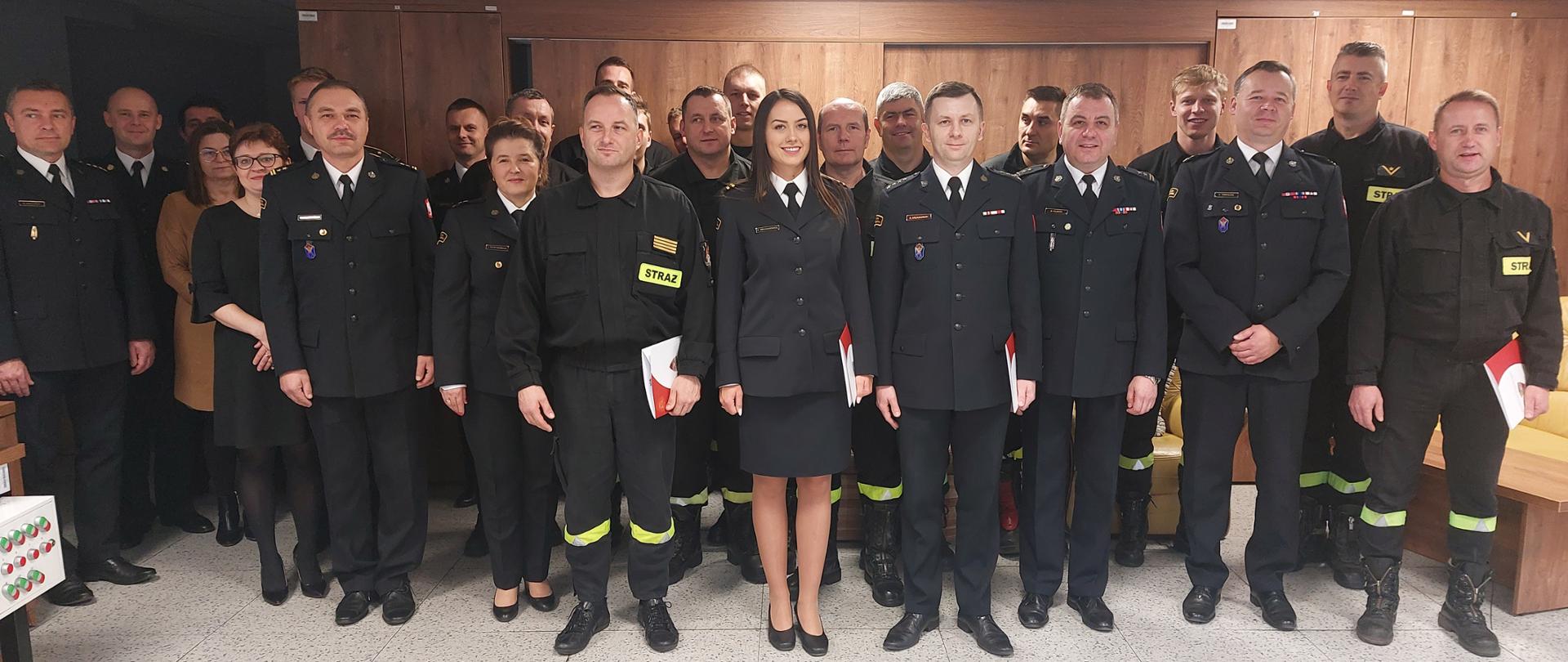 Zdjęcie przedstawia strażaków stojących w pomieszczeniu Stanowiska Kierowania Komendanta Miejskiego podczas wręczenia awansów.