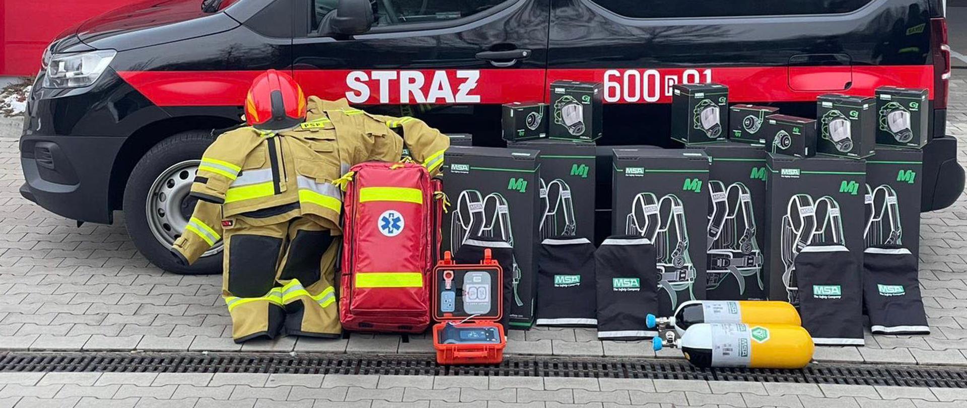 Na zdjęciu sprzęt na tle samochodu SLKw, aparaty OUO, butle, maski, AED torba R1 oraz ubranie specjalne i hełm strażacki