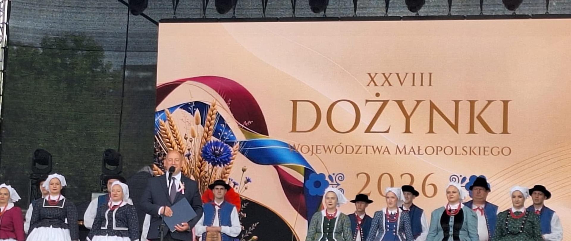 Grupa osób na scenie, w tle baner z napisem Dożynki województwa małopolskiego