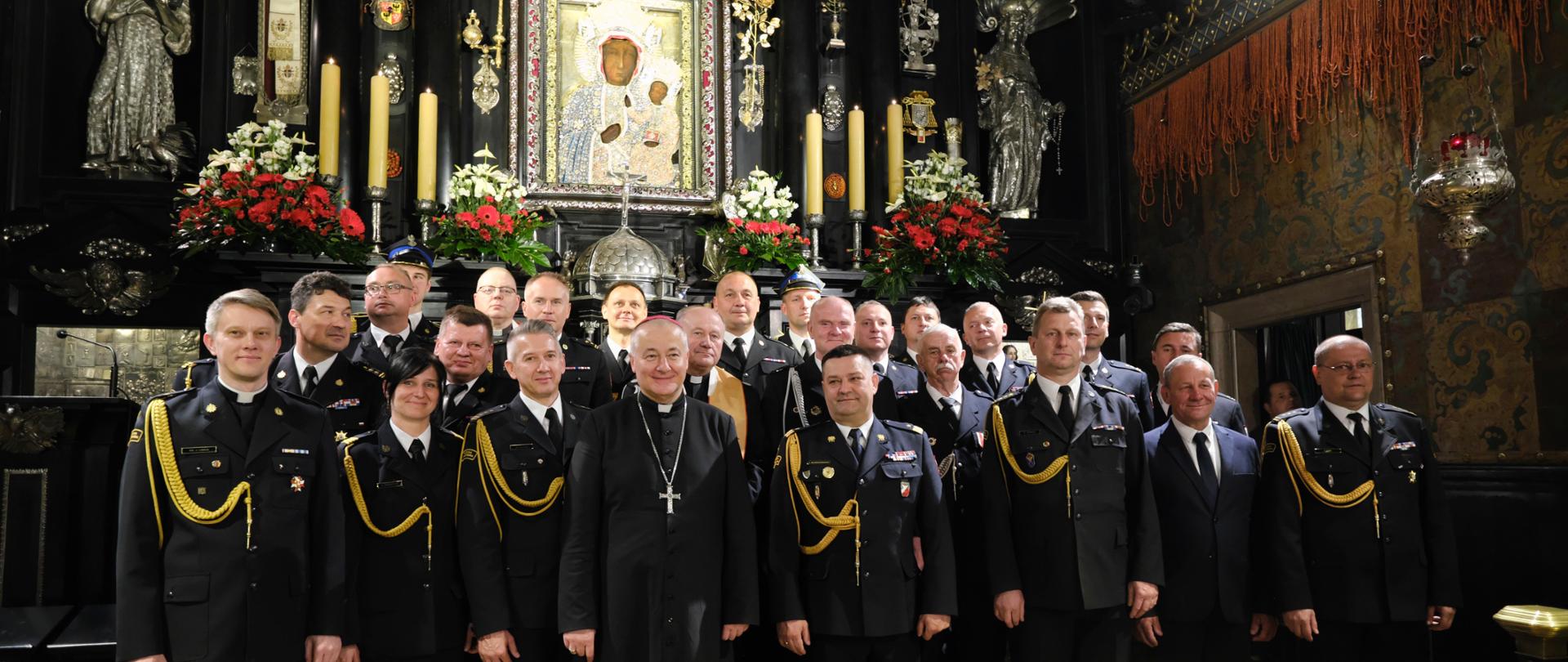 Zdjęcie grupowe strażaków w pomieszczeniu kaplicy w klasztorze podczas Apelu Jasnogórskiego w intencji strażaków Państwowej Straży Pożarnej i druhów Ochotniczych Straży Pożarnych oraz ich rodzin.
