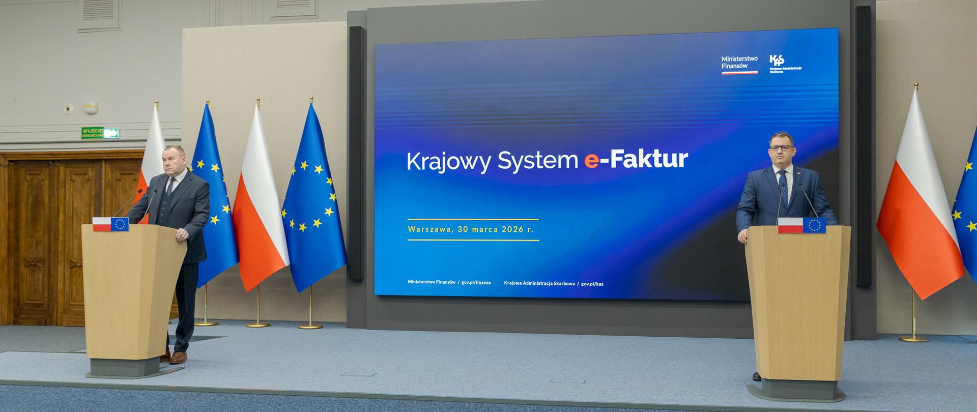 Konferencja prasowa, na której przemawiają dwaj mężczyźni. W tle baner Krajowy System e-Faktur oraz flagi Polski oraz Unii Europejskiej.