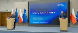 Konferencja prasowa, na której występuje dwóch mężczyzn. W tle baner Krajowego Systemu e-Faktur oraz flagi Polski i Unii Europejskiej.