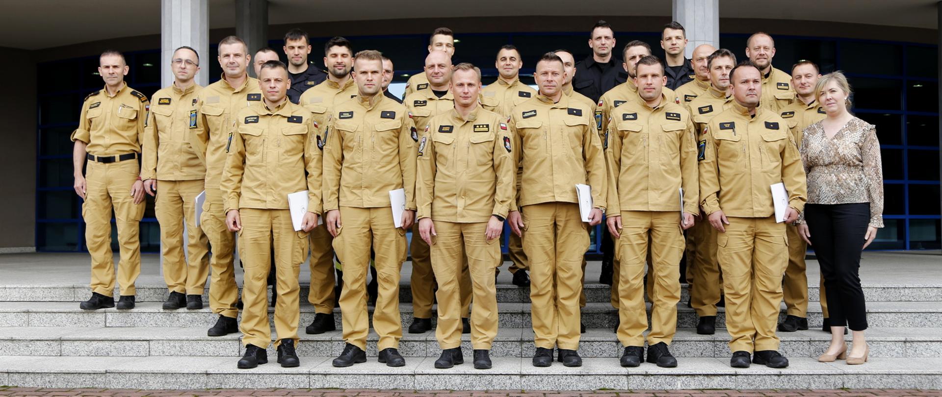 Grupowe zdjęcie uczestników szkolenia (20 funkcjonariuszy PSP) w towarzystwie Zastępcy Komendanta Centralnej Szkoły PSP, trzech oficerów CS PSP oraz kobiety