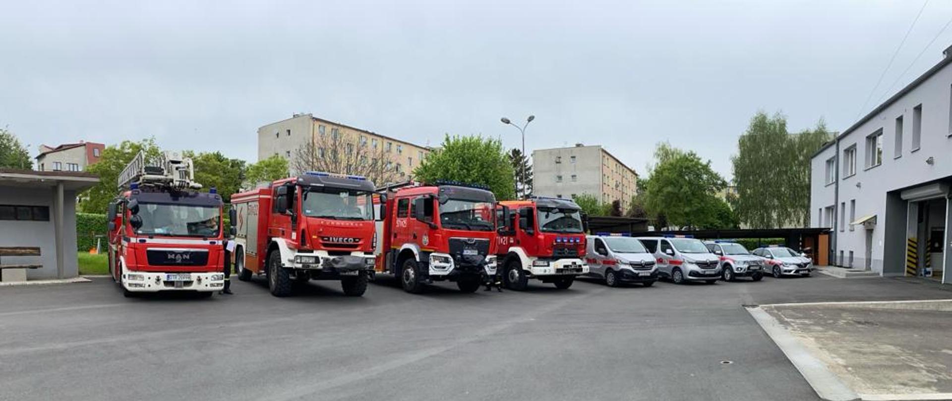 Ustawione obok siebie samochody bojowe, czerwone i samochody operacyjne, srebrne. Samochody ustawione na placu komendy