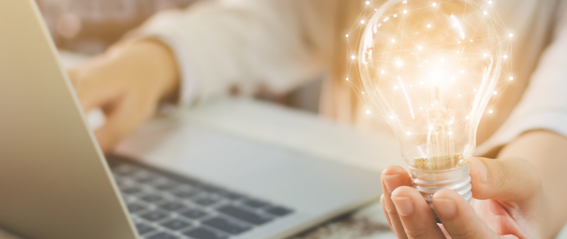 osoba jedną ręką pisze na laptopie a w drugiej trzyma świecącą żarówkę
