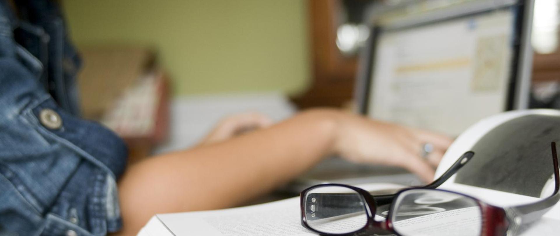 kobieta korzystająca z komputera, obok okulary korekcyjne