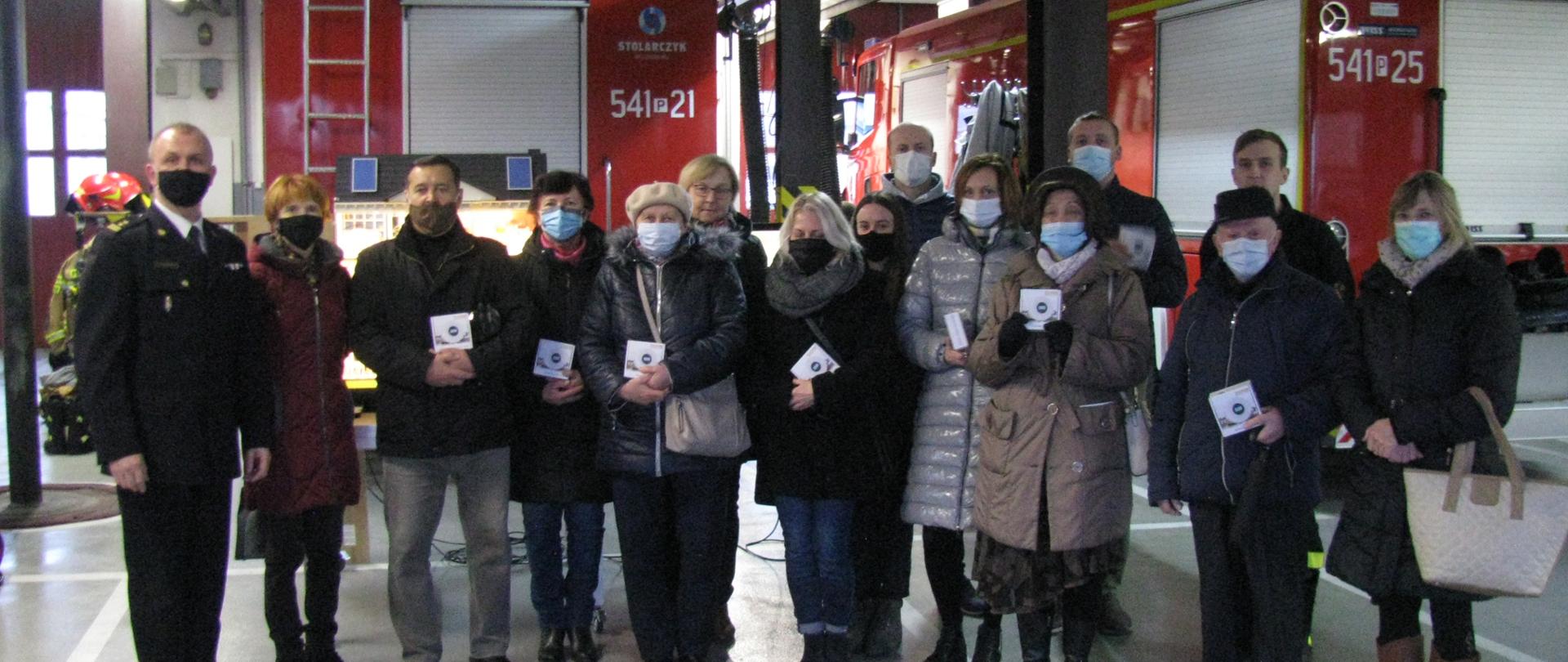 Na zdjęciu laureaci konkursu z komendantem powiatowym. Zdjęcie wykonane w garażu straży pożarnej. W tle wozy strażackie.