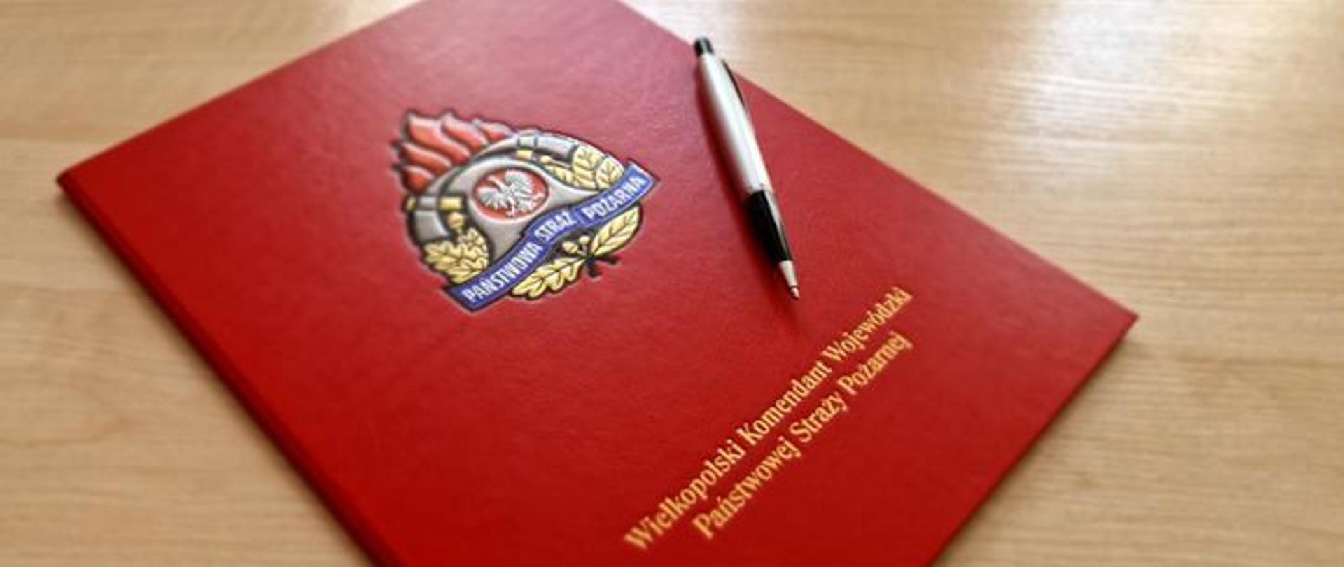 Zdjęcie przedstawia czerwoną teczkę na dokumenty z logiem PSP i napisem Wielkopolski Komendant Wojewódzki PSP