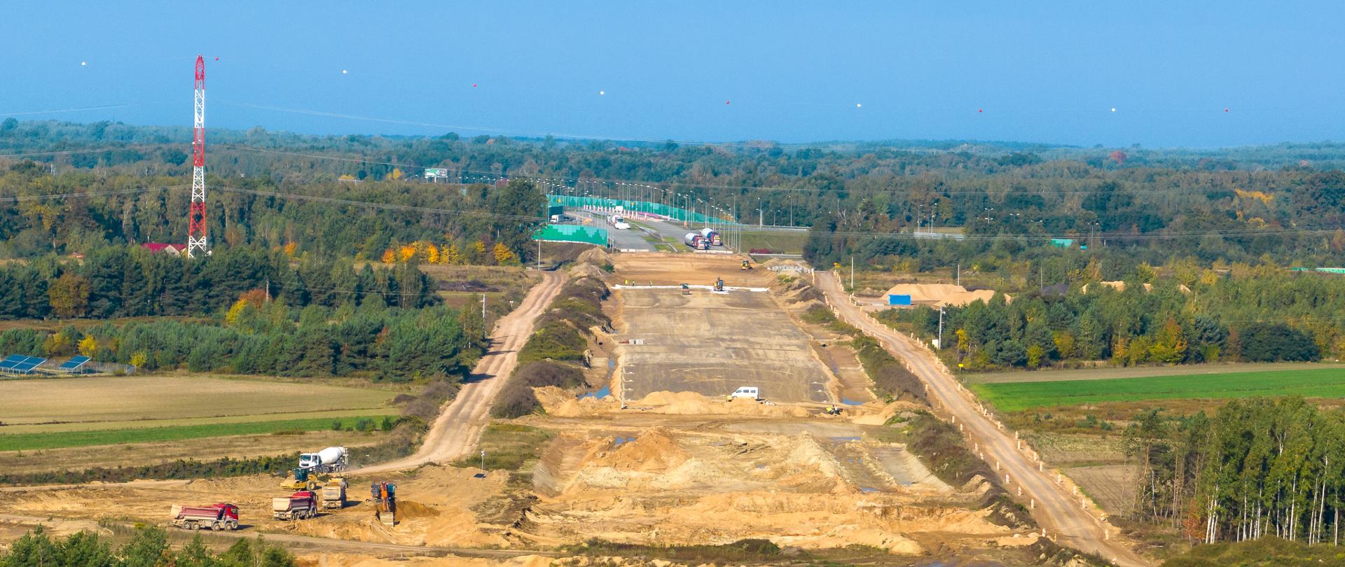 Widok na plac budowy autostrady A2. Wczesny etap prac. Widoczny szeroki pas oczyszczonej ziemi i przygotowanej podbudowy pod nową autostradę. W tle, na horyzoncie widoczne już gotowe pasy ruchu.