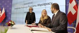 Minister funduszy i polityki regionalnej Grzegorz Puda i sekretarz stanu ds. gospodarki Szwajcarii Helene Budliger Artieda siedzą przy stole i podpisują umowę na drugą edycję Szwajcarsko-Polskiego Programu Współpracy, po lewej stoi Ewa Lineburg z BM MFiPR 