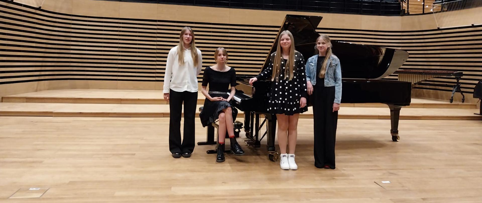Cztery dziewczyny stoją przy fortepianie.