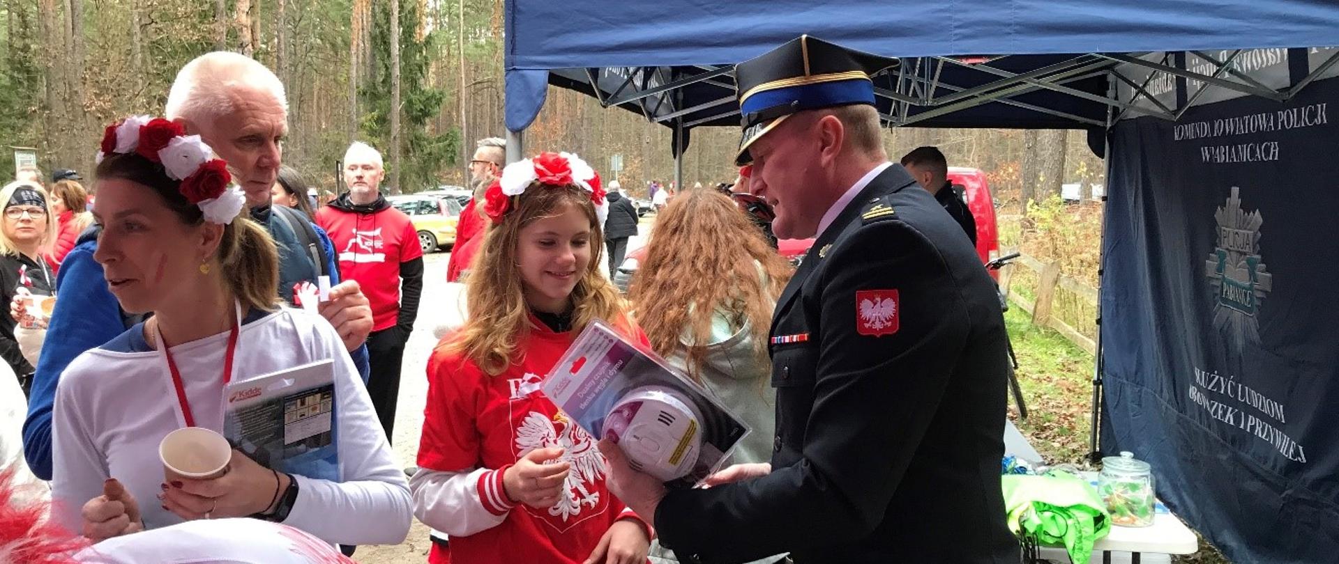 Na zdjęciu Zastępca Komendanta Powiatowego PSP w Pabianicach wręcza jednej z uczestniczek pikniku wylosowaną dualną czujkę tlenku węgla i dymu. 
