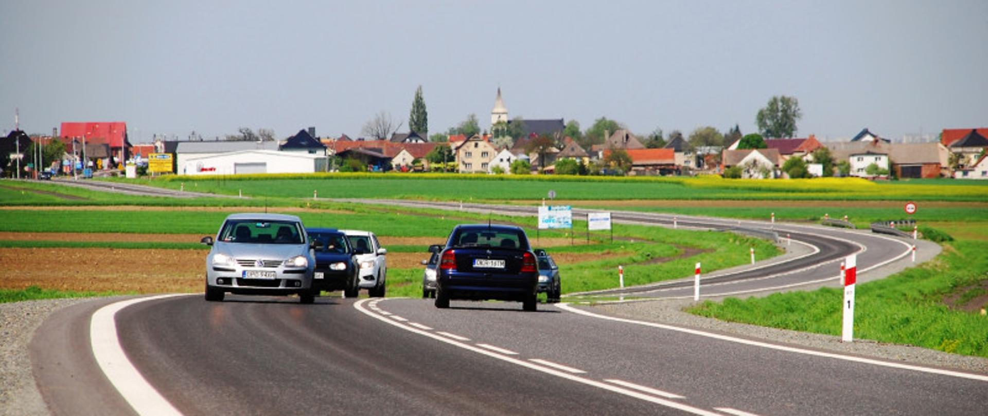 Asfaltowa droga z zakrętami , na niej pojazdy jadące w przeciwnych kierunkach 