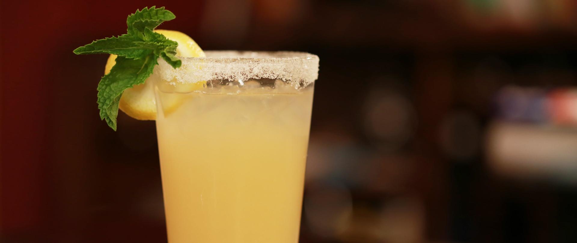 Fotografia przedstawiająca szklankę z napojem z lodem i plasterkiem cytryny umieszczonym na brzegu szklanki