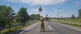 Zdjęcie zdrobnione w dzień na drodze krajowej. Na zdjęciu widać strażaka, który przyjmuje śmigłowiec LPR. 