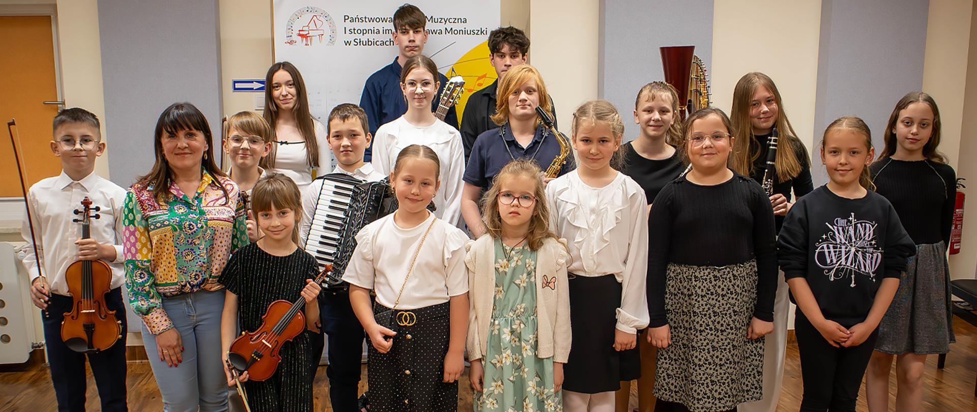 Grupa kilkunastu uczniów wraz z Dyrektorką stoją w auli na tle baneru szkolnego.