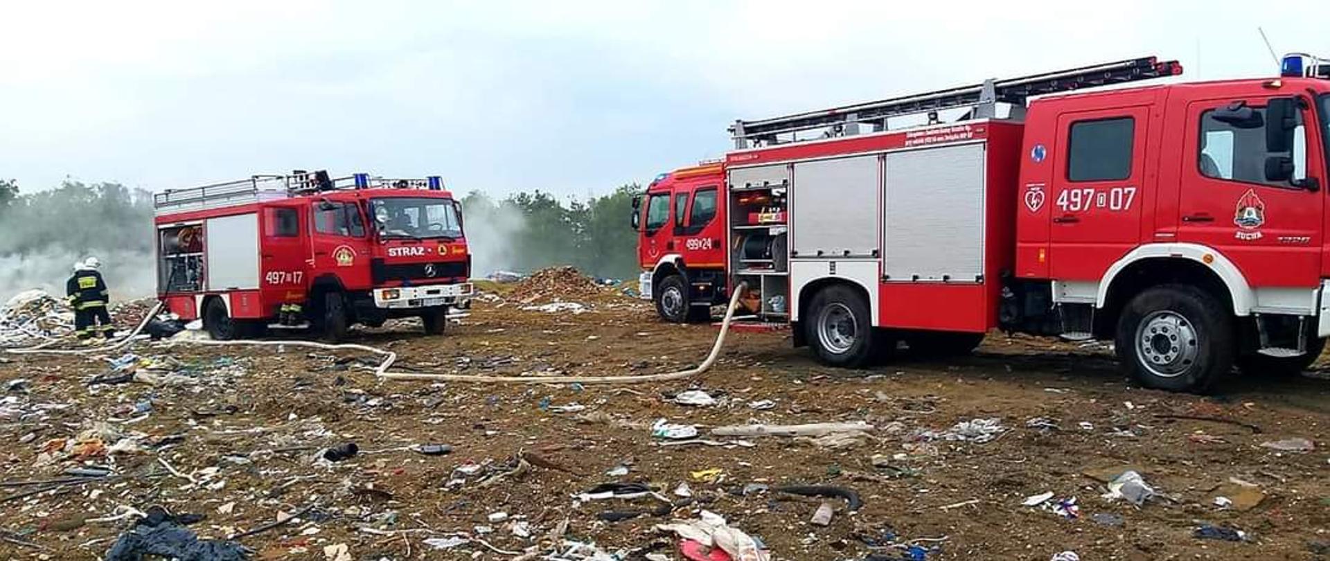 Zdjęcie przedstawia dwa samochody pożarnicze podczas gaszenia pożaru składowiska odpadów