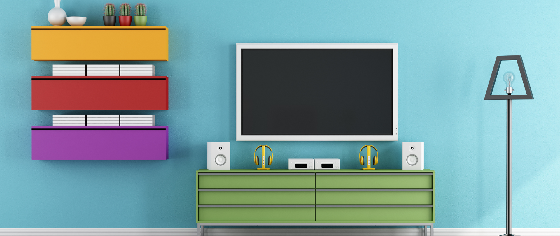 Telewizor wiszący na ścianie. Pod nim komoda, a na niej słuchawki oraz głośniki. Obok kolorowe wiszące półki oraz srebrna lampa