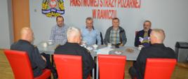 Narada z kominiarzami i zarządcami budynków wielorodzinnych. Świetlica KP PSP w Rawiczu. Przy wspólnym stole siedzi trzech funkcjonariuszy komendy, a na przeciwko nich czterech mężczyzn . Dwaj z nich to mistrzowie kominiarscy, pozostali - zarządcy budynków wielorodzinnych w Rawiczu. W tle na ścianie logo PSP i napis "Komenda Powiatowa PSP w Rawiczu" Na stole filiżanki z kawą, ciastka, talerzyki.