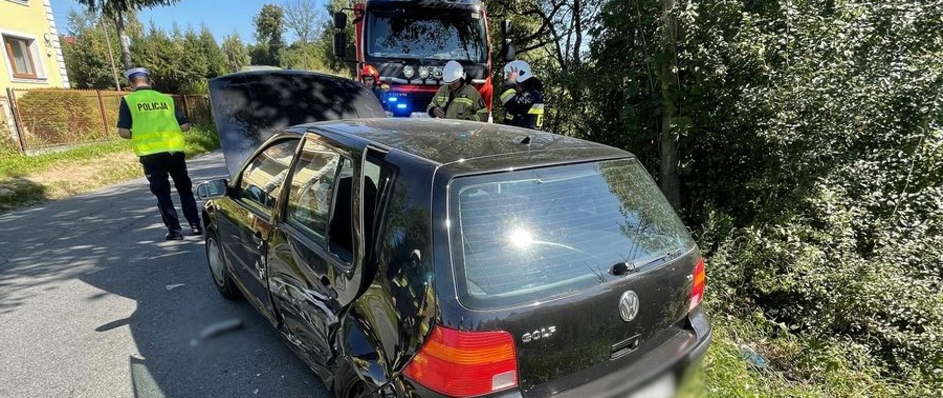 Samochód osobowy na poboczu. Obok policjant a w tle samochód pożarniczy.