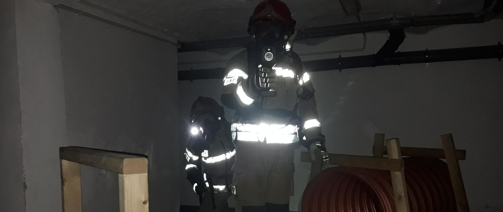 Ciemno, strażacy w aparatach, piwnica.