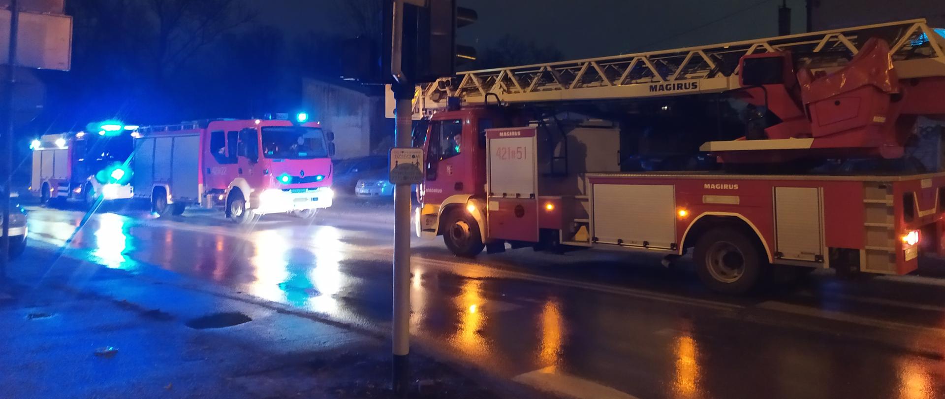 Zdjęcie przedstawia 3 wozy strażackie stojących na ulicy z włączonymi sygnałami świetlnymi