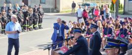 zastępca mazowieckiego komendanta wojewódzkiego psp przemawia podczas uroczystości. z boku widać orkiestrę dęta, po drugiej stronie stoją młodzi strażacy osp.