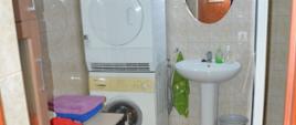 Miejsca noclegowe w siedzibie OSP. Pomieszczenie łazienki, w którym znajduje się umywalka, pralki automatyczne oraz stół. Na stole leżą ręczniki. Nad umywalką zawieszone jest lustro.