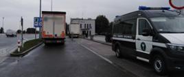 Na pierwszym planie (od prawej): przód i prawy bok oznakowanego furgonu małopolskiej ITD. W tle: tył dwóch zestawów ciężarowych zatrzymanych do kontroli przez inspektorów ITD i budynek komisariatu autostradowego Policji.