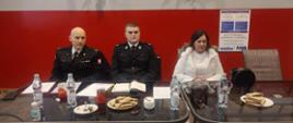 Na zdjęciu widać siedzących na zebraniu OSP w remizie w Wojnowice strażaków dwóch ubranych w mundury oraz Panią burmistrz Ćmielowa. Przed siedzącymi stolik z przekąskami oraz wodą.