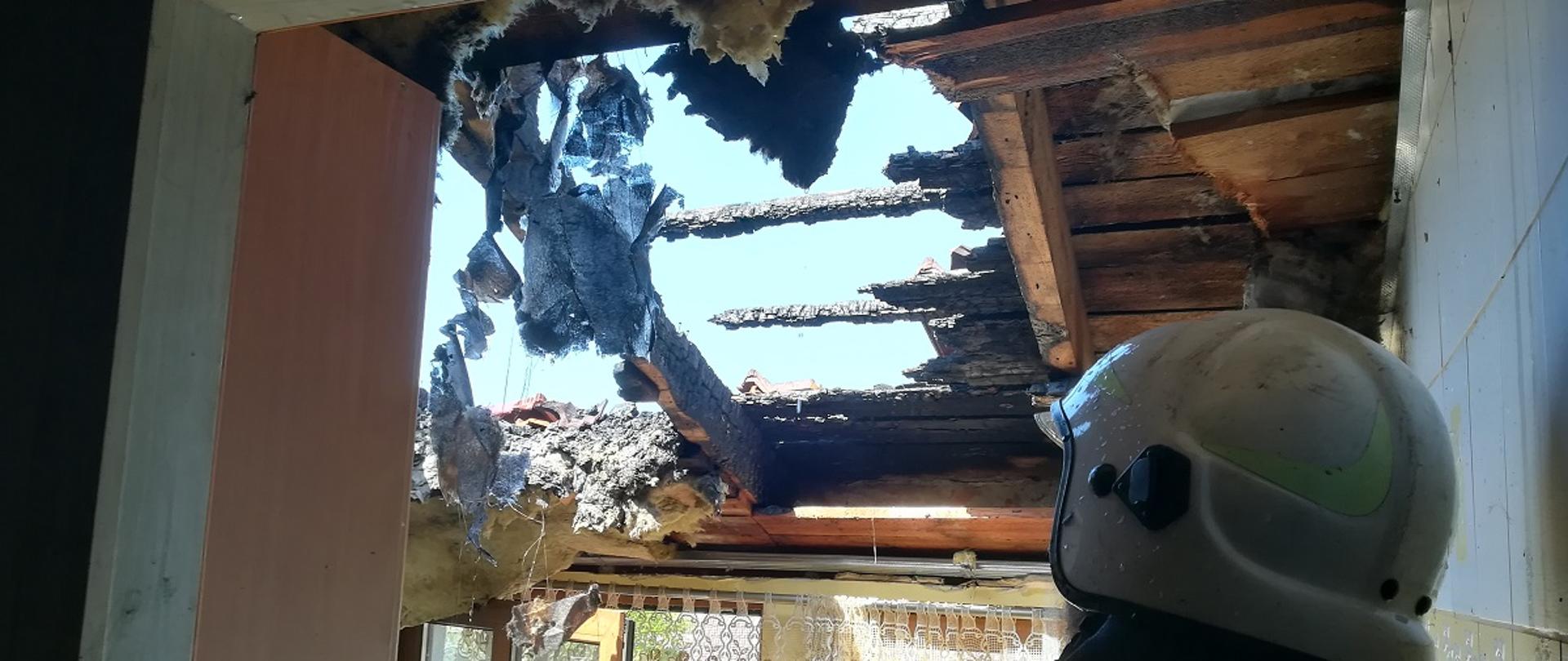 Strażak w białym hełmie w spalonym domu patrzący na wypaloną dziurę w suficie