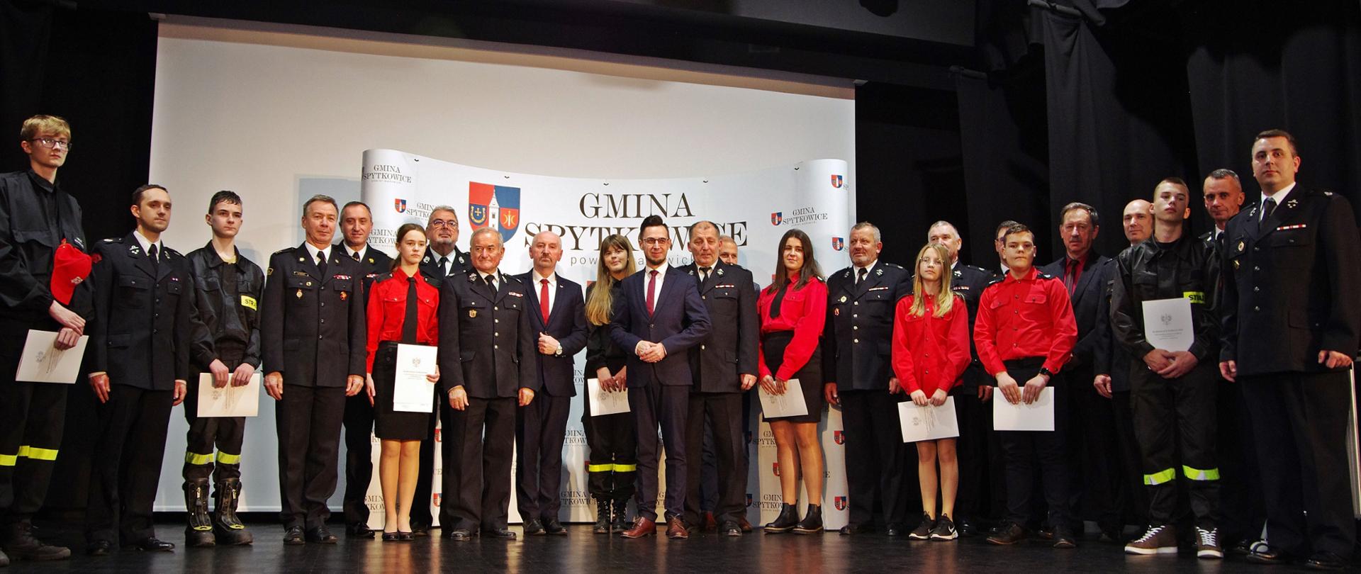 Widok sceny z przodu. Zdjęcie grupowe przedstawicieli OSP z gośćmi honorowymi.