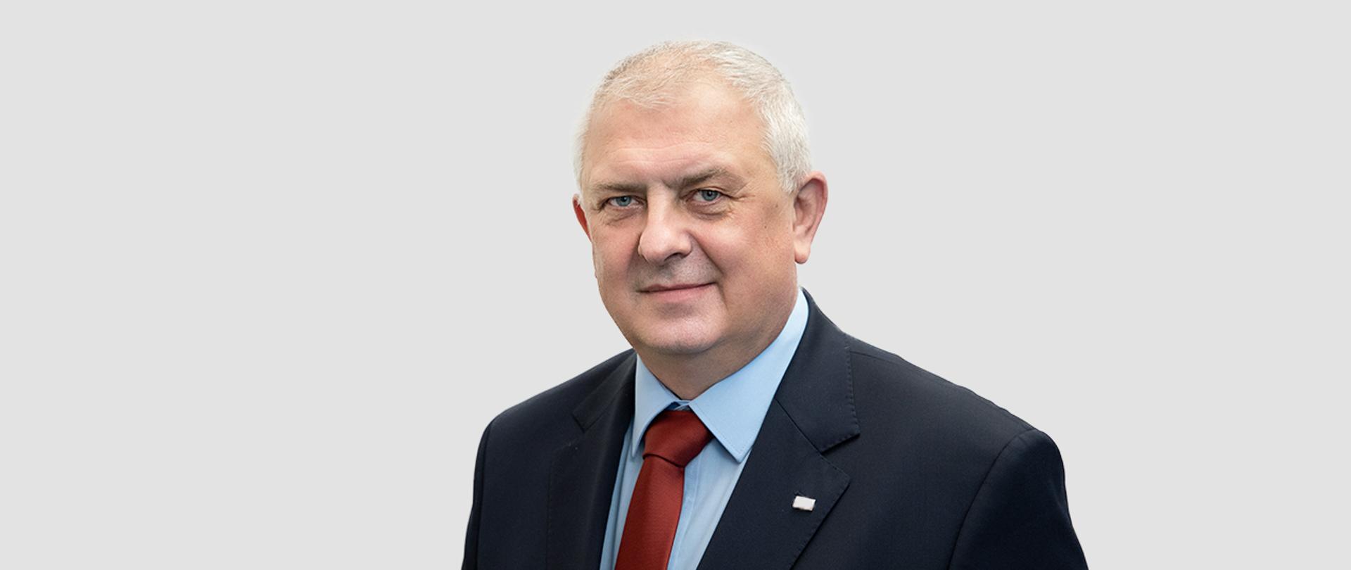 Sekretarz Stanu Grzegorz Piechowiak, w garniturze, z czerwonym krawatem