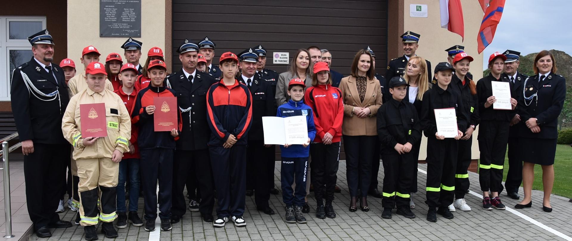 Na zdjęciu widzimy wszystkich uczestników uroczystości ustawionych do zdjęcia grupowego przed budynkiem remizy OSP Surochów.