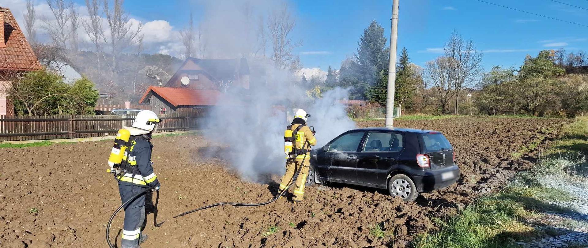 Strażacy gaszą pożar samochodu na polu ornym